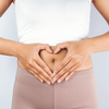 The mid section of a woman with her hands over her tummy in a heart shape. She is wearing active wear with a white top and light pink leggings.